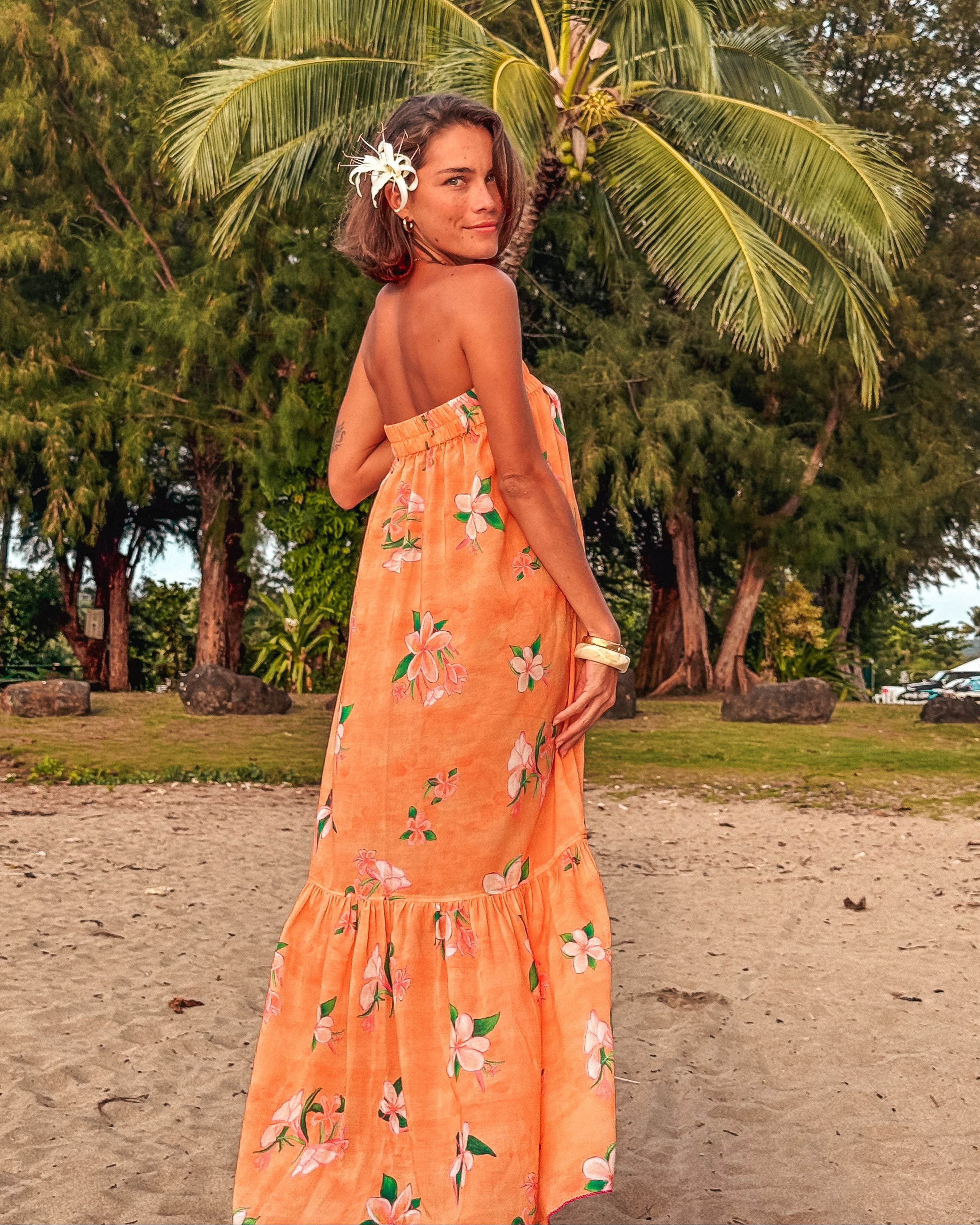 Woman in an orange floral dress standing on a beach with palm trees in the background